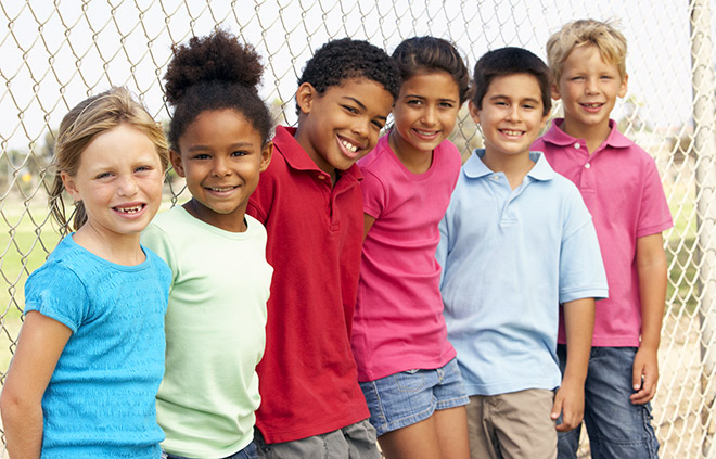 Different children smiling and standing next to a fence